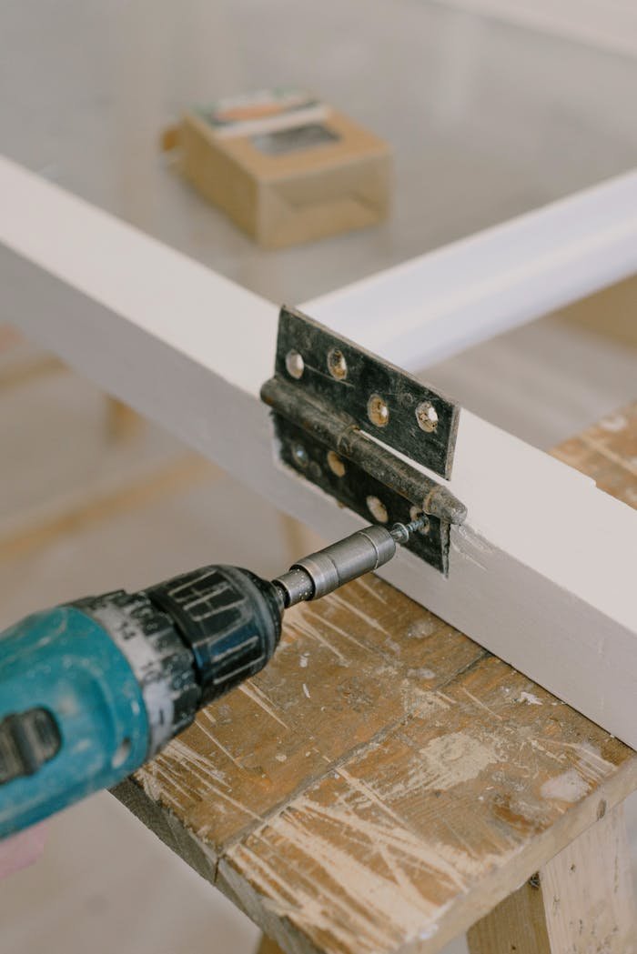 Close-up of an electric drill installing a door hinge on a wooden workbench.